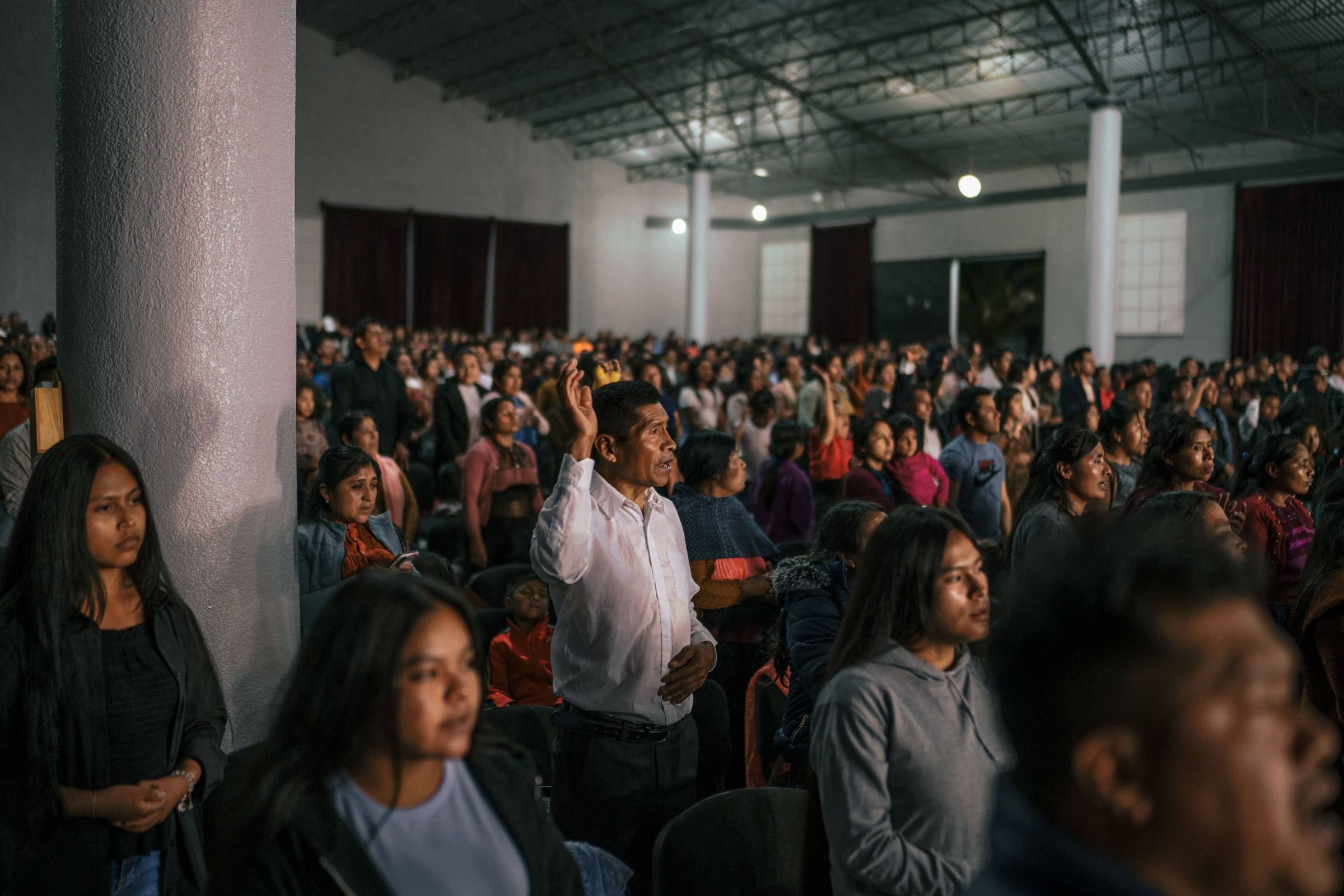 Un hombre levanta la mano en oración en un templo lleno.