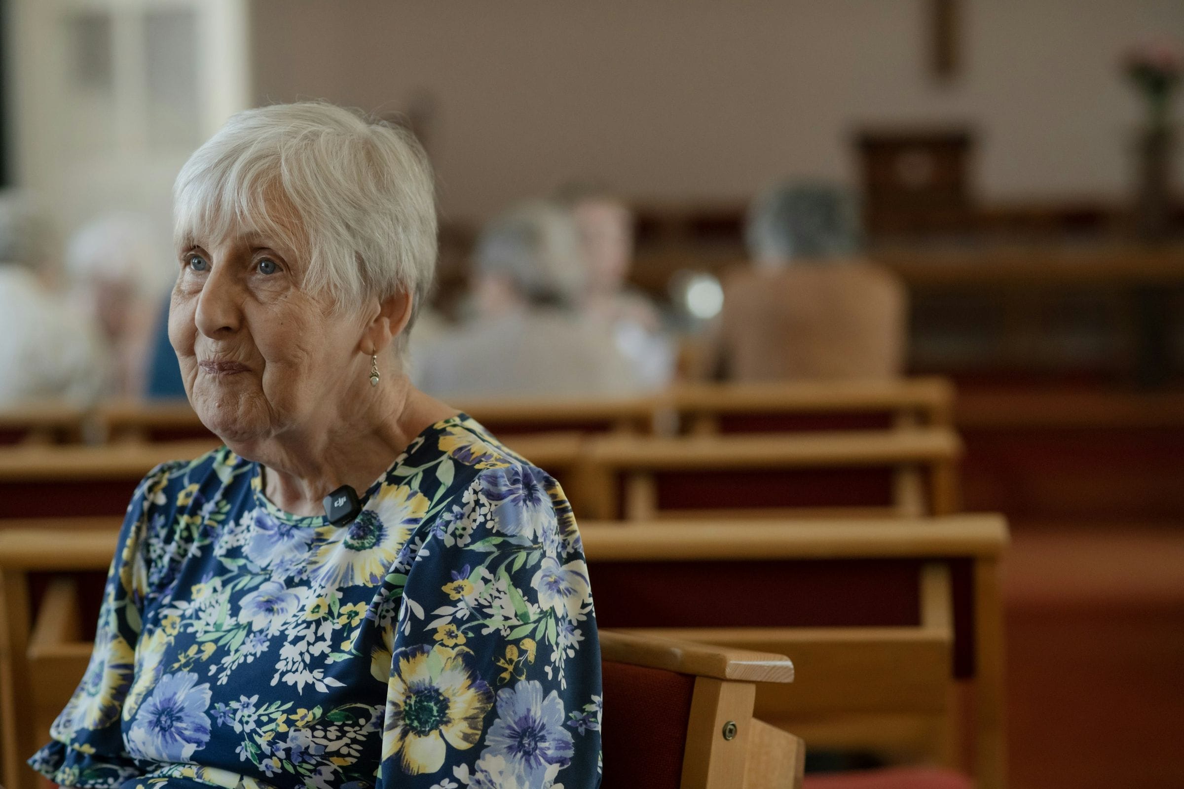 Una mujer mayor escucha desde un banco de la iglesia.