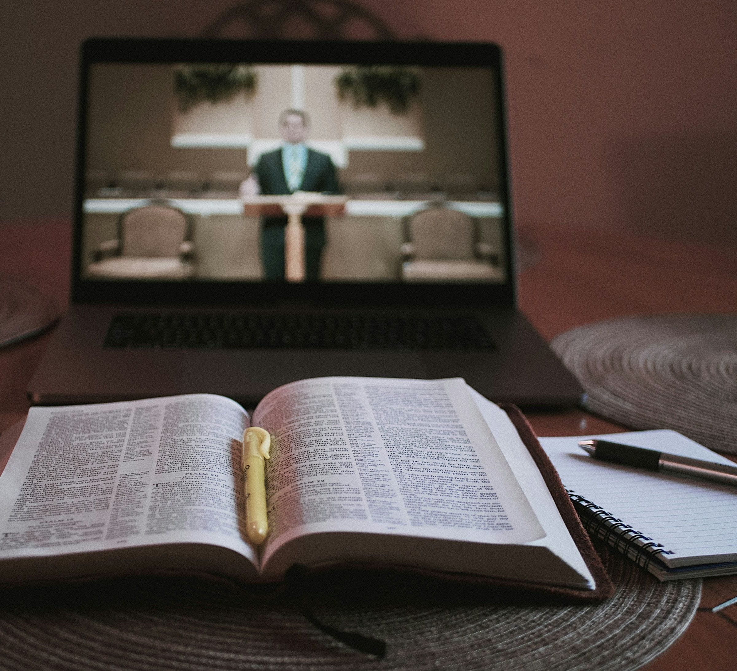Una laptop reproduce un sermón grabado junto a una Biblia abierta y un cuaderno.